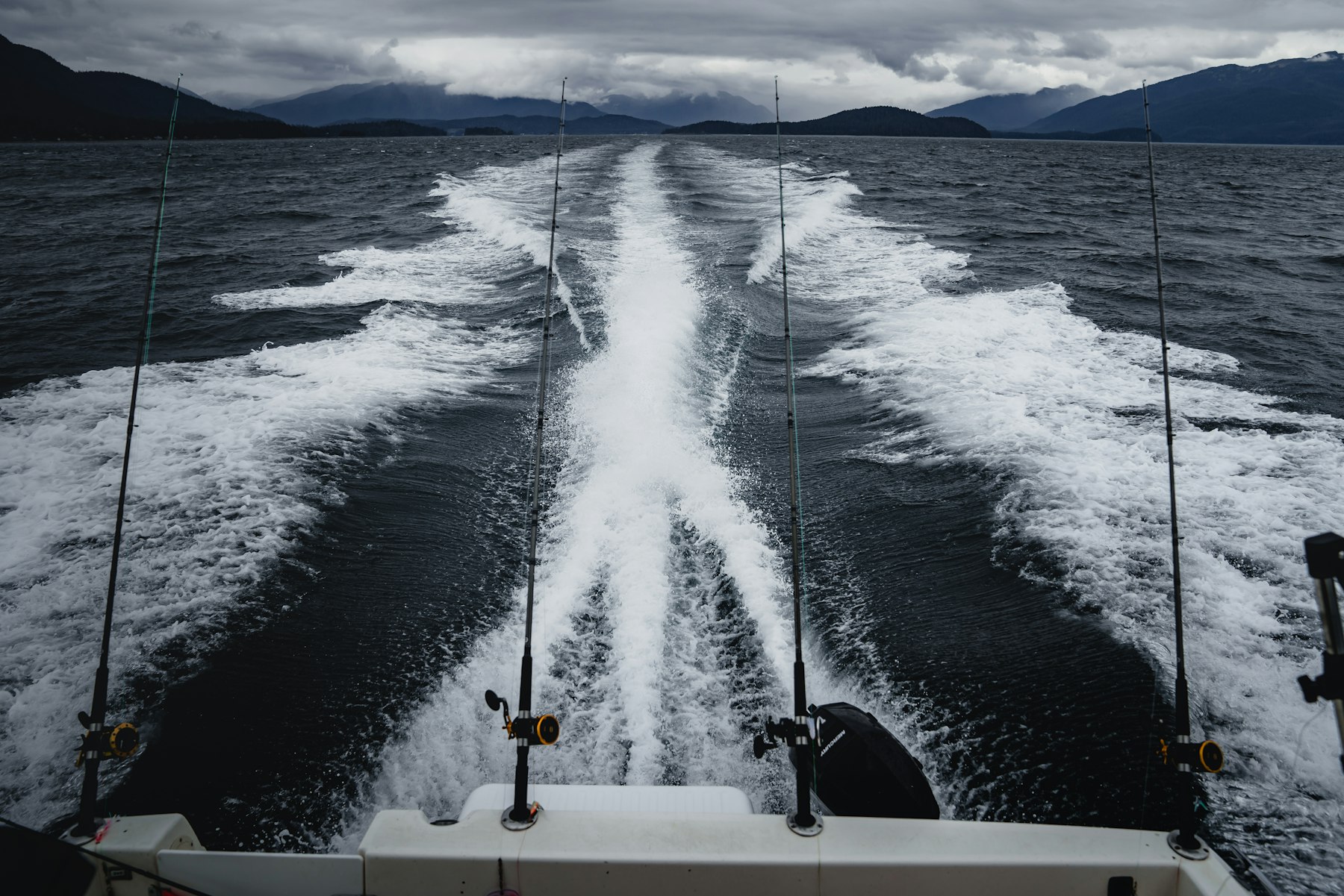The wake and rods trailing behind a fishing boat under moody Haida Gwaii skies