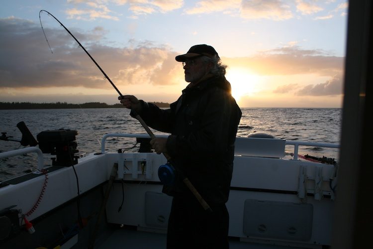 An angler working a rod against a Haida Gwaii sunset from the deck of a boat